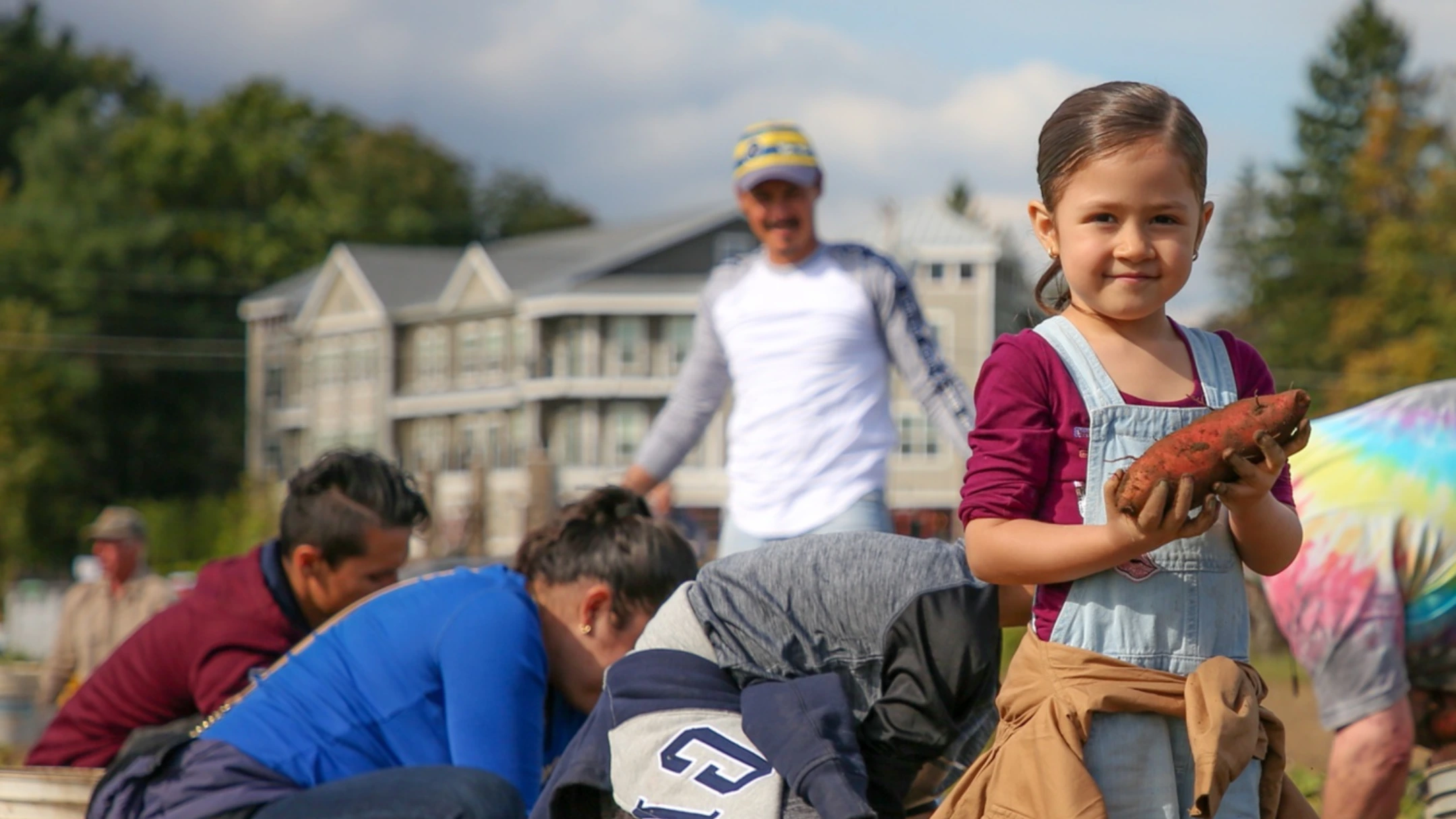 A girl holding a freshly dug sweet potato at a community garden harvest
